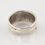Breiter Metallschlichter Ring mit matter Oberfläche und leichten Gebrauchsspuren auf weiß reflektierendem Hintergrund.