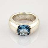 Breiter silberner Ring mit kissenförmigem, facettiertem blauen Edelstein und polierter Oberfläche