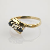 Goldring mit asymmetrischem Band und drei Steinen, zwei dunkelblau und einem klaren, auf weißem Eleganter Goldring mit gebogenem Steinbesatz aus zwei dunkelblauen und einem weißen Edelstein.