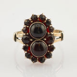 Eleganter Goldring mit zwei ovalen dunklen Steinen und kleineren facettierten dunkelroten Steinen in floraler Anordnung.