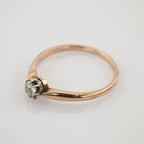 Feiner Goldring mit kleinem Diamant in Silberfassung auf reflektierender weißer Oberfläche
