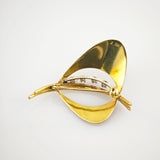 Goldene Brosche mit zwei geschwungenen Flügeln und zentraler Stange mit Edelsteinen.