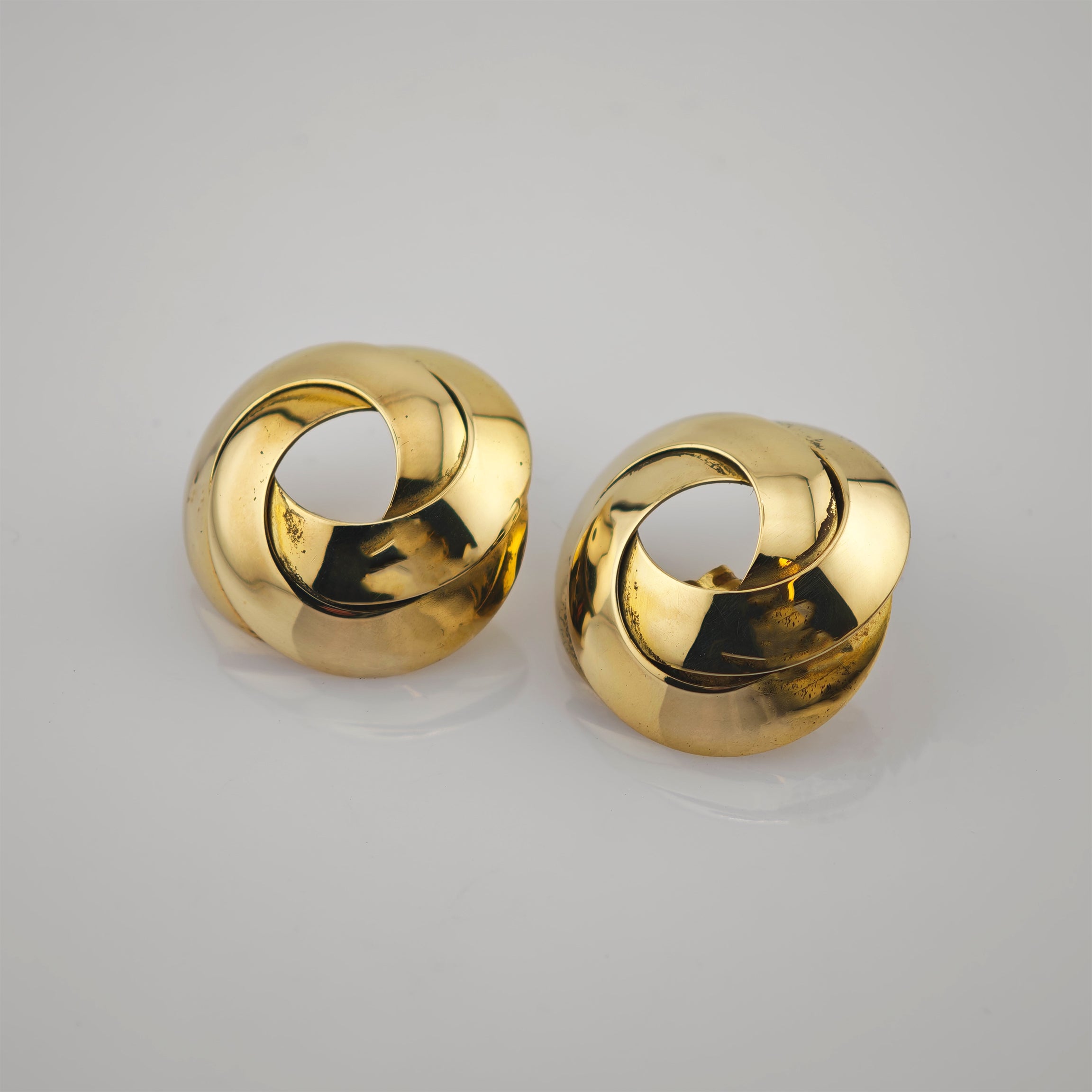 Paar goldene Ohrringe mit elegant gedrehtem offenem Runddesign auf grauem Hintergrund