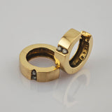 Zwei goldene Ringe mit flachem Band und kleinen Diamanten auf spiegelnder Oberfläche.