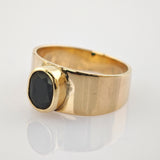 Goldener Ring mit breitem Band und ovalem schwarzen Edelstein auf reflektierender Oberfläche