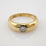 Goldener Ring mit rundem Band und Einzel-Diamanten auf reflektierender weißer Oberfläche