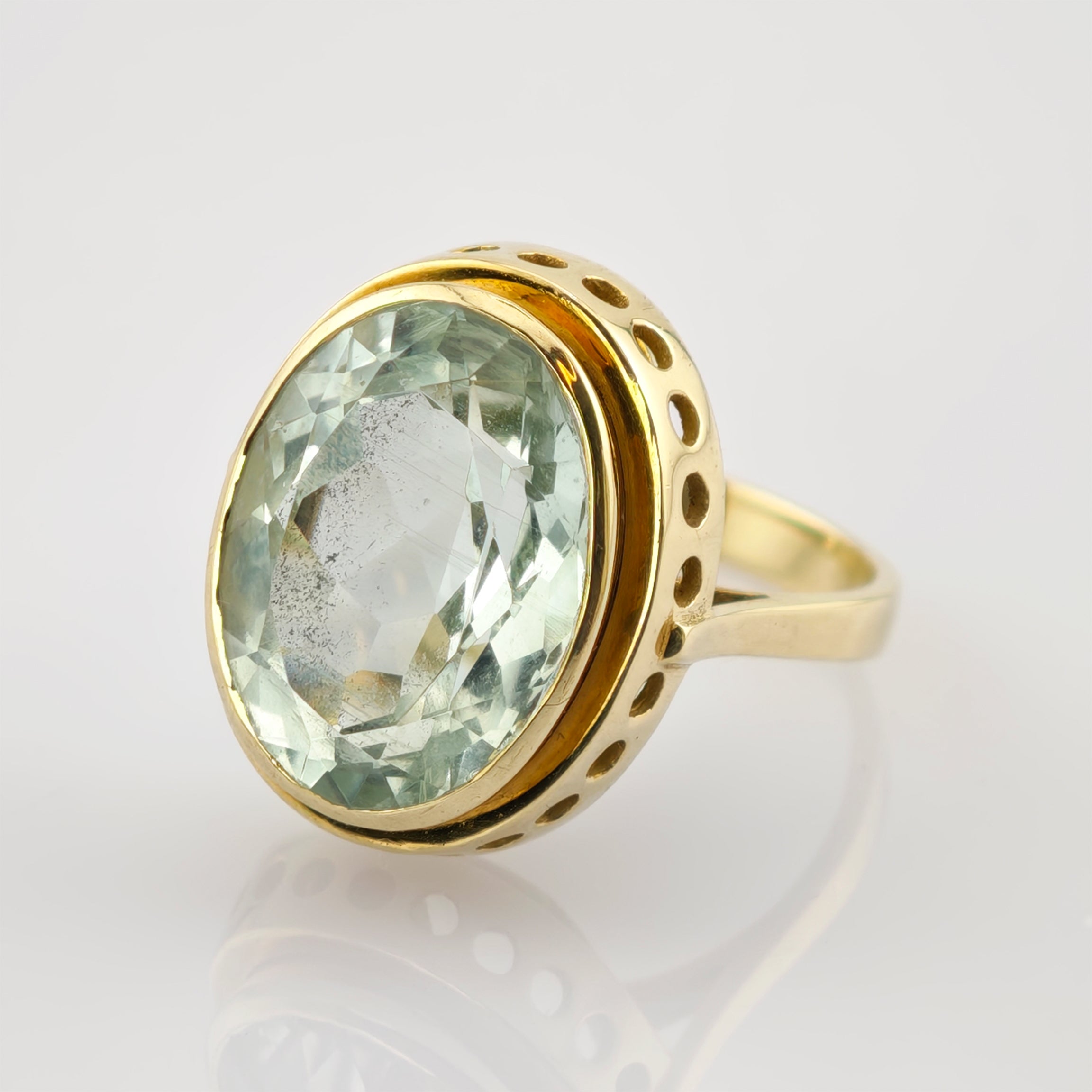 Goldener Ring mit ovalem, hellgrünem facettierten Edelstein und runden Ausschnitten im Design.