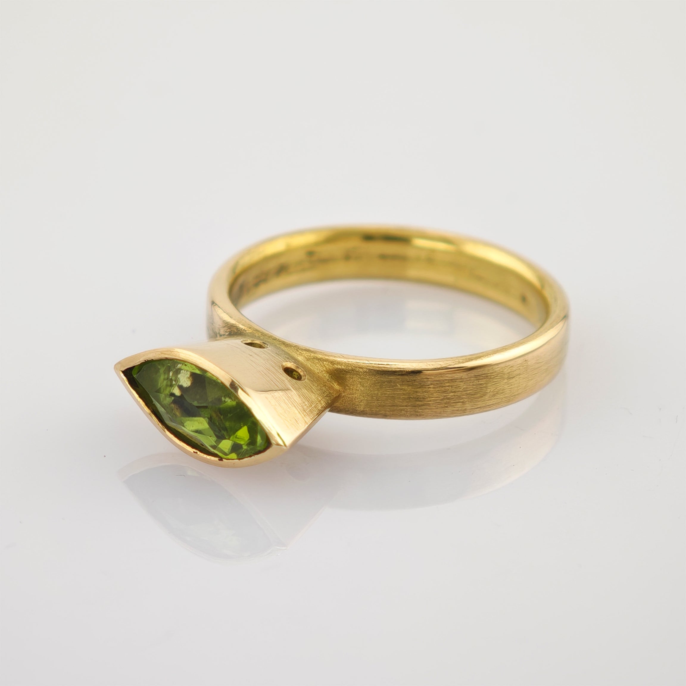 Goldener Ring mit matt gebürstetem Band und grünem Marquise-Edelstein im Facettenschliff.
