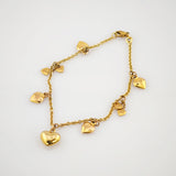 Feines goldfarbenes Armband mit Kette und kleinen herzförmigen Anhängern auf weißem Hintergrund.