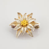 Goldfarbene Brosche in Form einer achtblättrigen Blume mit Netzmuster und strukturiertem Zentrum im Vintage-Stil.