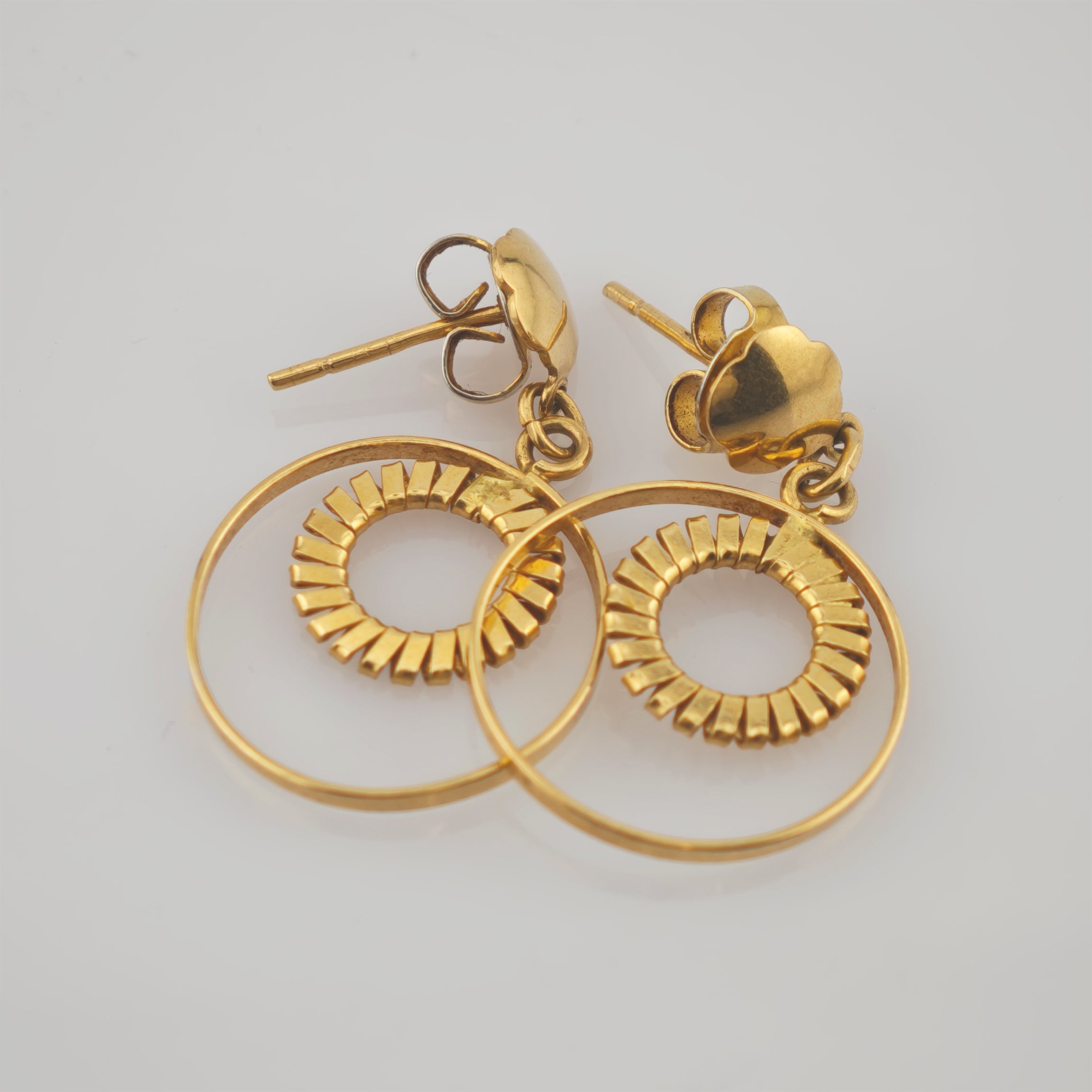 Goldfarbene Ohrstecker mit kleinen, kreisförmigen Ringen und Schmetterlingsverschlüssen auf hellem Untergrund.