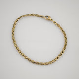 Goldfarbenes gedrehtes Seilarmband aus poliertem Metall mit Karabinerverschluss auf weißem Hintergrund.