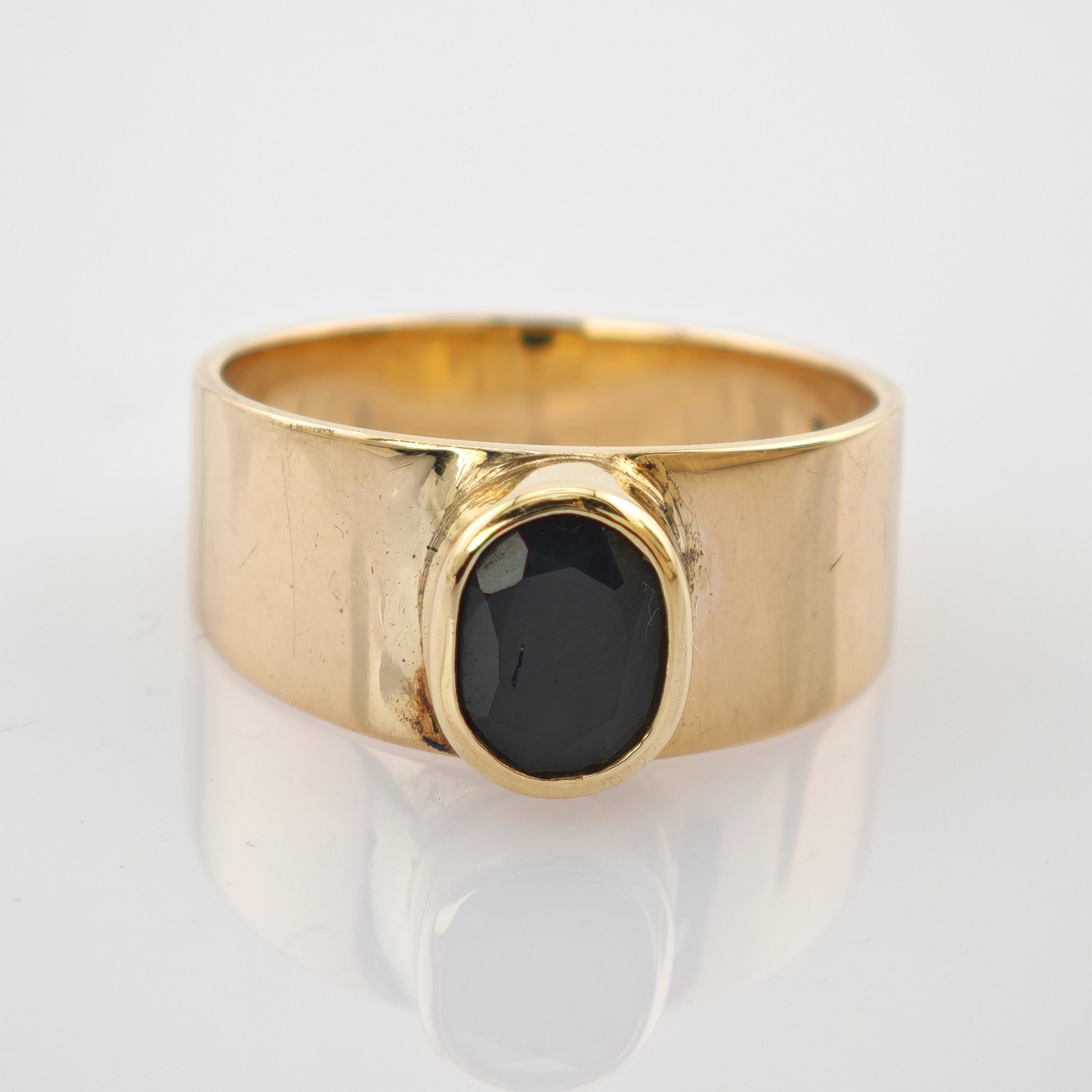 Goldring mit breitem Band und ovalem facettiertem schwarzen Edelstein in Goldfassung auf weißem Hintergrund.
