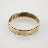 Goldener Hochzeitsring mit gezacktem Muster auf spiegelnder weißer Goldring mit einfacher geschwungener Musterkante und leichten Gebrauchsspuren auf weißer Oberfläche