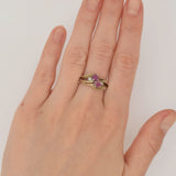 Hand mit goldfarbenem Ring und violetten Edelsteinen vor weißem Hintergrund