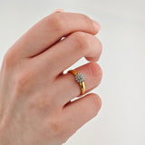 Hand mit Goldring am Ringfinger mit floralem Diamantcluster vor weißem Hintergrund