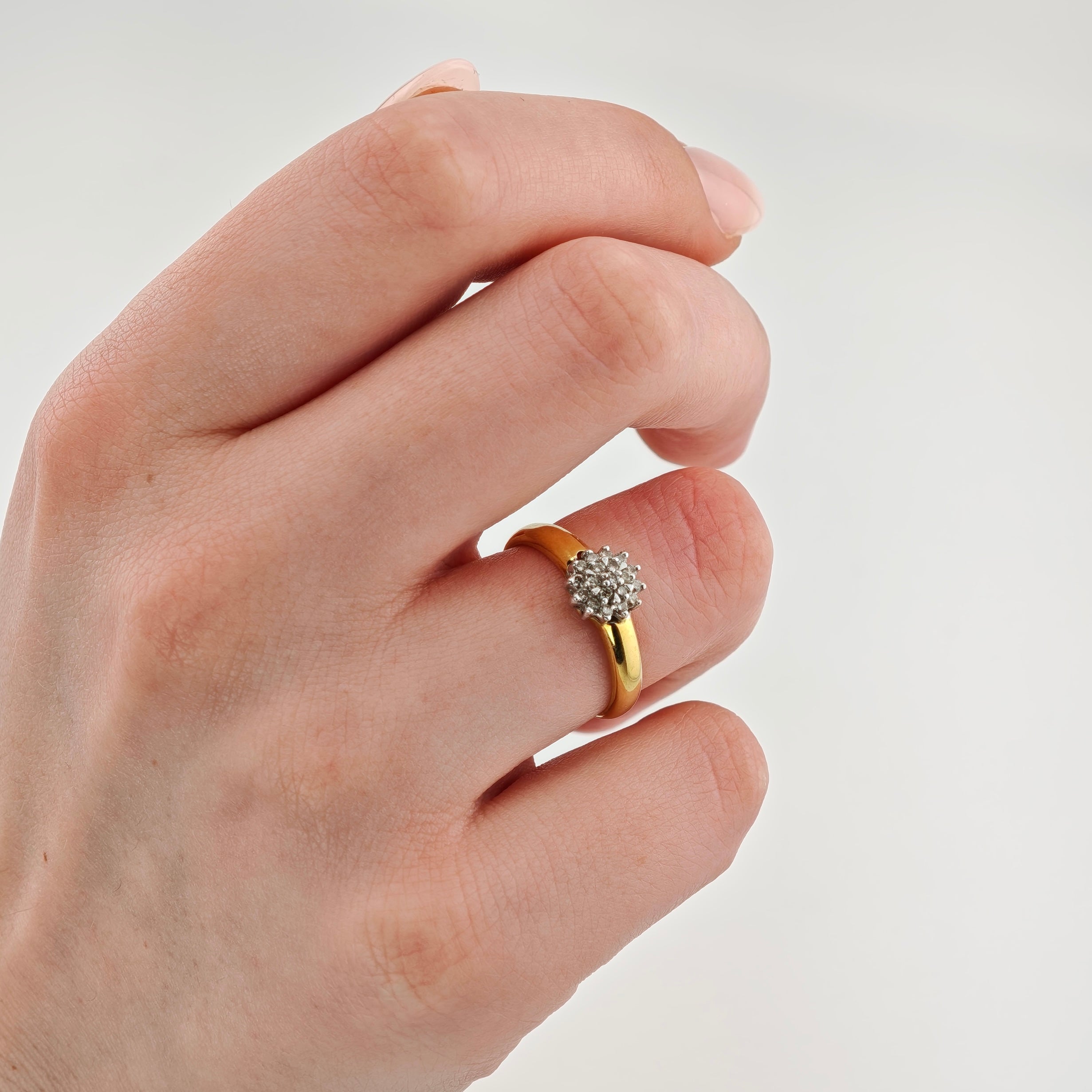 Hand mit Goldring am Ringfinger mit floralem Diamantcluster vor weißem Hintergrund