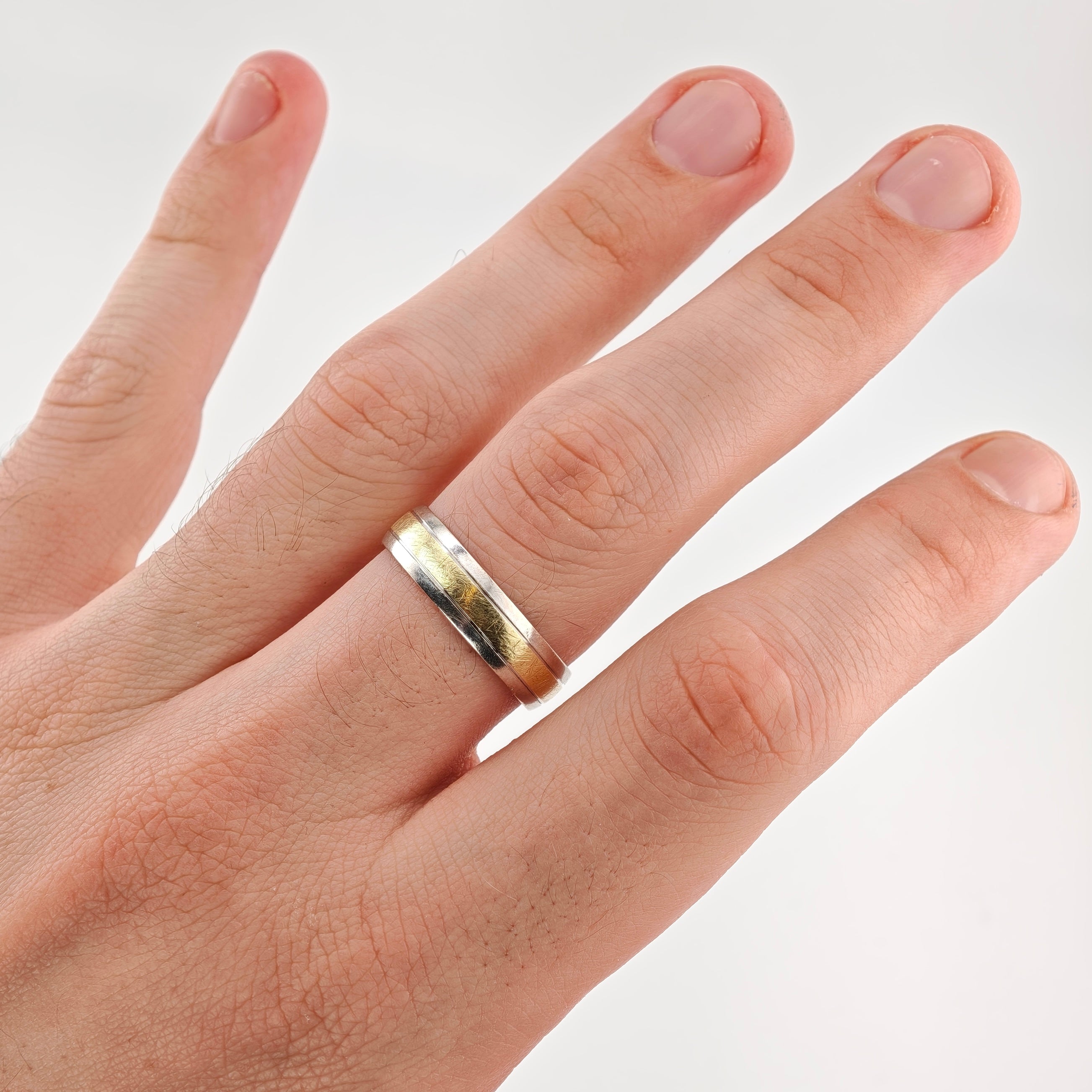 Hand mit silber-goldenem Ehering am Ringfinger vor weißem Hintergrund