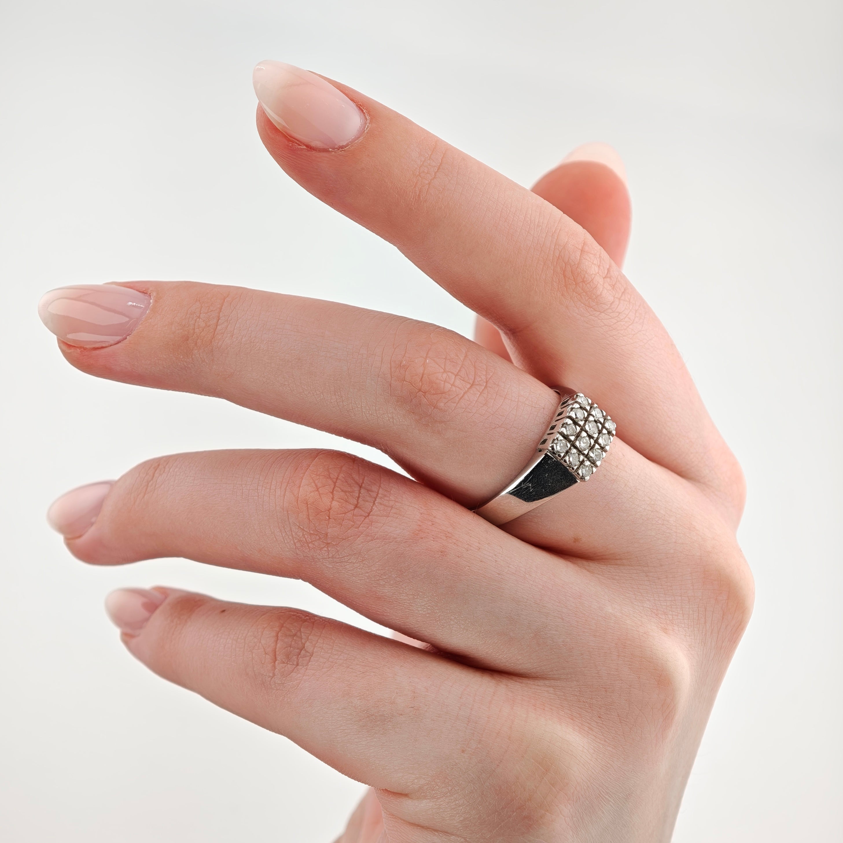 Hand mit quadratischem Silberring und Diamantmuster auf mittlerem Finger vor weißem Hintergrund