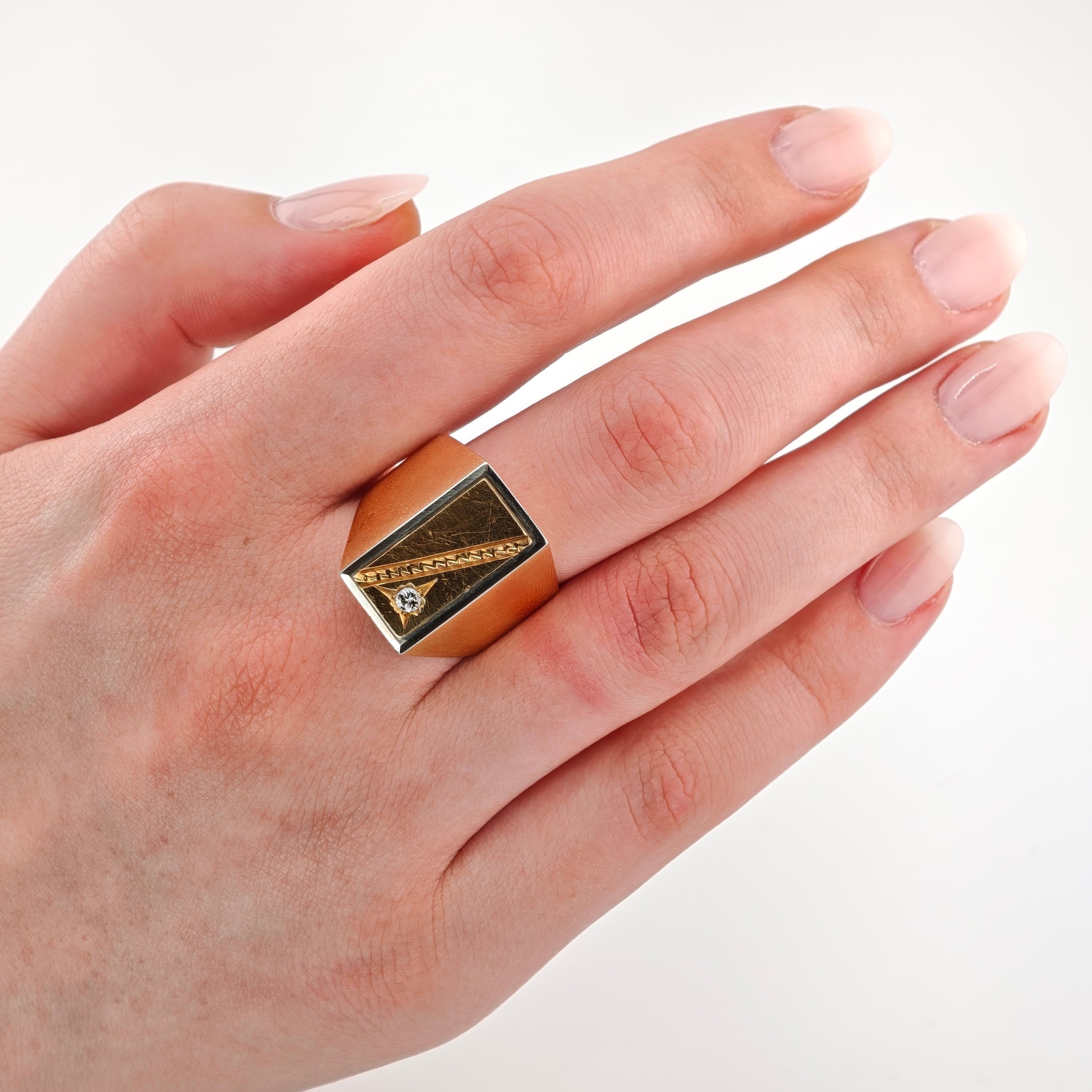 Hand mit gepflegten, rosa lackierten Nägeln mit geometrischem goldfarbenem Ring und kleinem klaren Edelstein