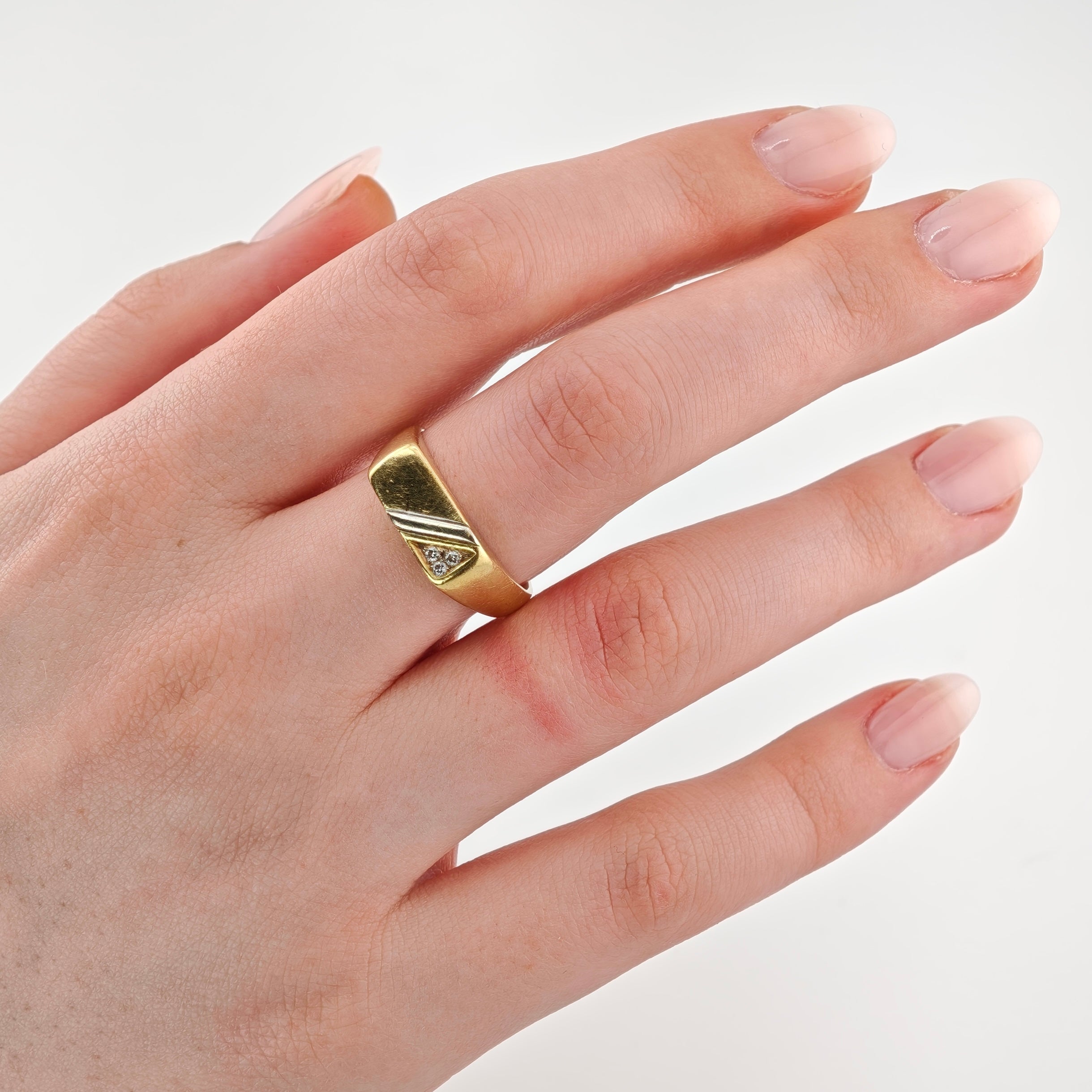 Linke Hand mit hellrosa lackierten Nägeln trägt einen goldenen Ring mit rechteckiger Platte und Diamant.