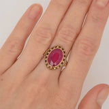Linke Hand mit Goldring am Mittelfinger mit großem ovalem tiefrosa facettiertem Edelstein und verzierten Ringdetails.