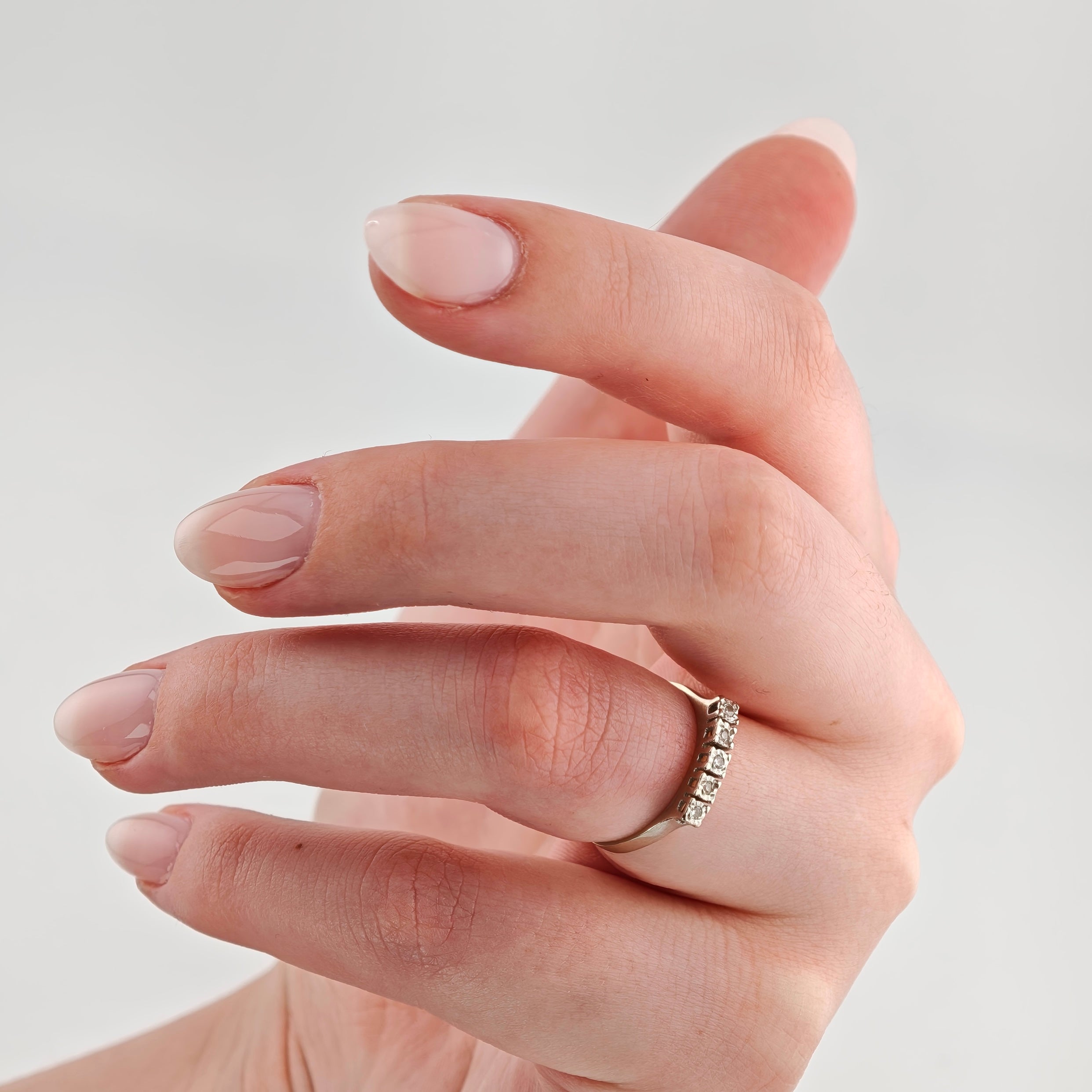 Linke Hand mit nudefarben lackierten Nägeln und silbernem Ring mit Diamanten.