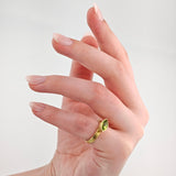 Linke Hand mit eleganten mandelförmigen rosa Nägeln und goldenem Ring mit grünem Marquise-Schliff Edelstein.