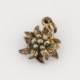 Kleiner Metallanhänger in Form einer stilisierten Blume mit acht texturierten Blättern und schwarz-goldener Patina.