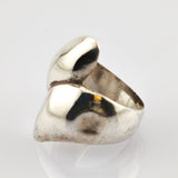 Polierter Metallschmuckring mit abstrakter, asymmetrischer Form auf weißem Hintergrund.