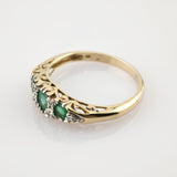 Goldener Ring mit filigraner Gravur und drei horizontal angeordneten Smaragden, umgeben von kleinen weißen Steinen.