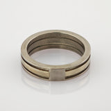 Zweiseitiger Metallring mit silbernem Außenband und goldenem Innenband auf reflektierender Oberfläche