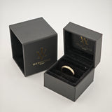 Schwarze samtige Schmuckbox mit Goldring und klaren Steinen, neben passender Verpackung mit Goldlogo auf weißem Hintergrund.