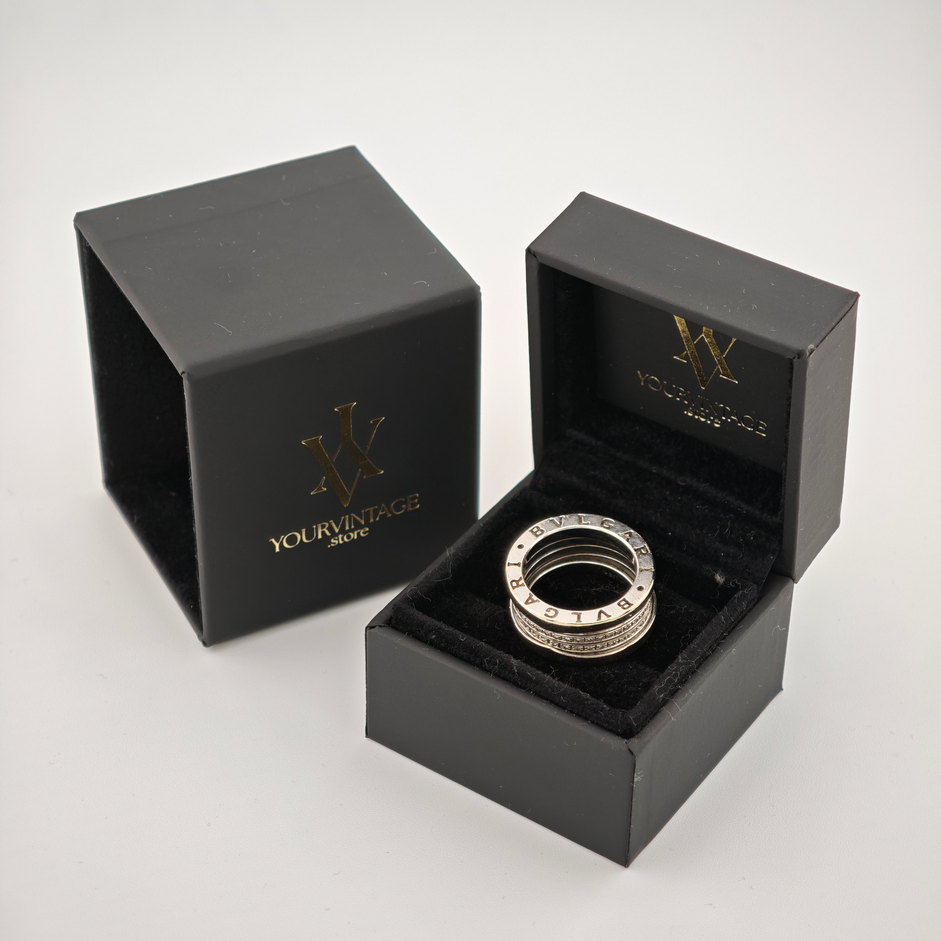 Zwei schwarze Schmuckboxen mit goldener Aufschrift "yourvintoge.shop" und stilisiertem W-Logo. Eine Box zeigt einen silbernen BVLGARI-Ring auf schwarzem Samtkissen.
