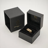 Schwarze Schmuckschachtel mit Goldring auf schwarzem Samt, daneben verzierte Außenschachtel mit Goldlogo auf weißem Hintergrund.