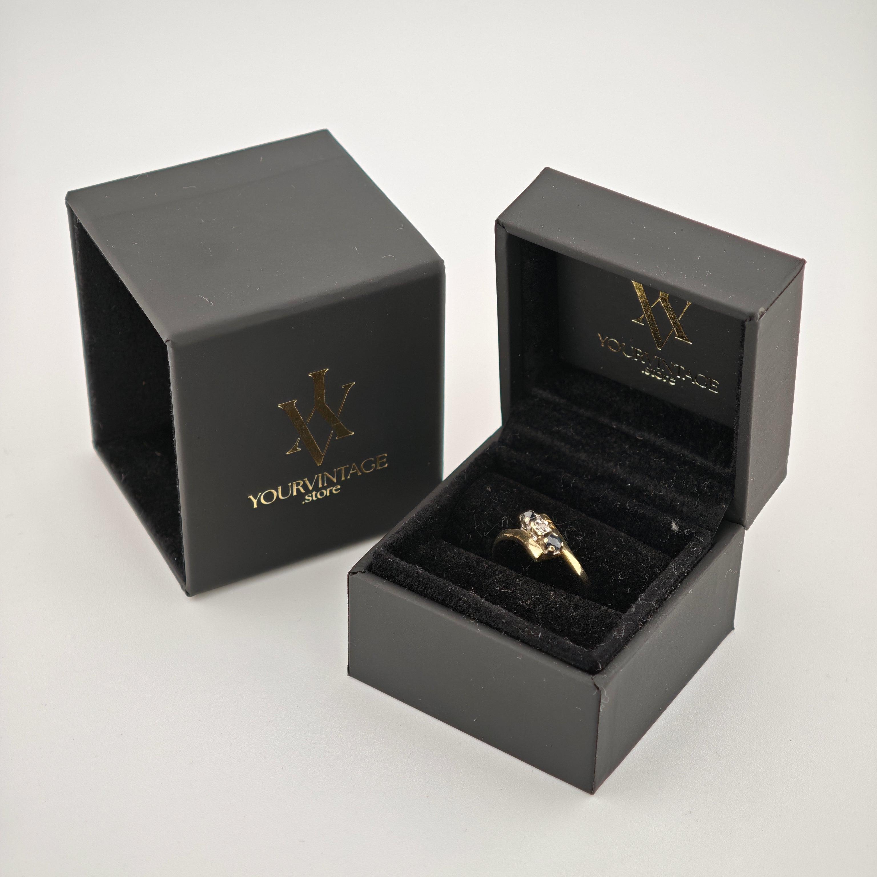 Schwarze Schmuckschachteln mit goldenem yourvintoge.shop-Schriftzug, eine offen mit goldfarbenem Ring auf schwarzem Samt.
