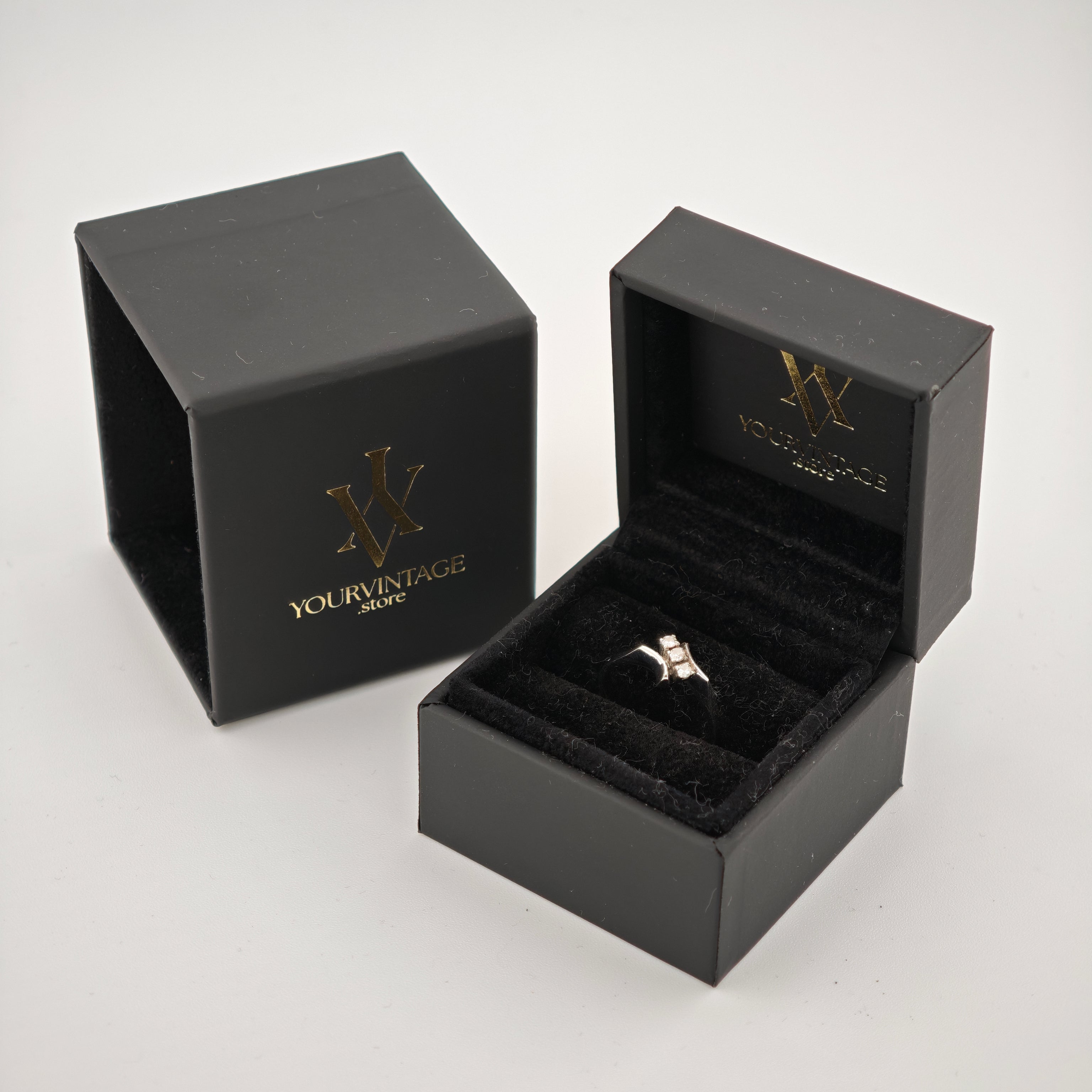 Geöffnete schwarze Schmuckbox mit Silberring und drei quadratischen Steinen, daneben geschlossene Box mit "yourvintoge.shop" Goldprägung.