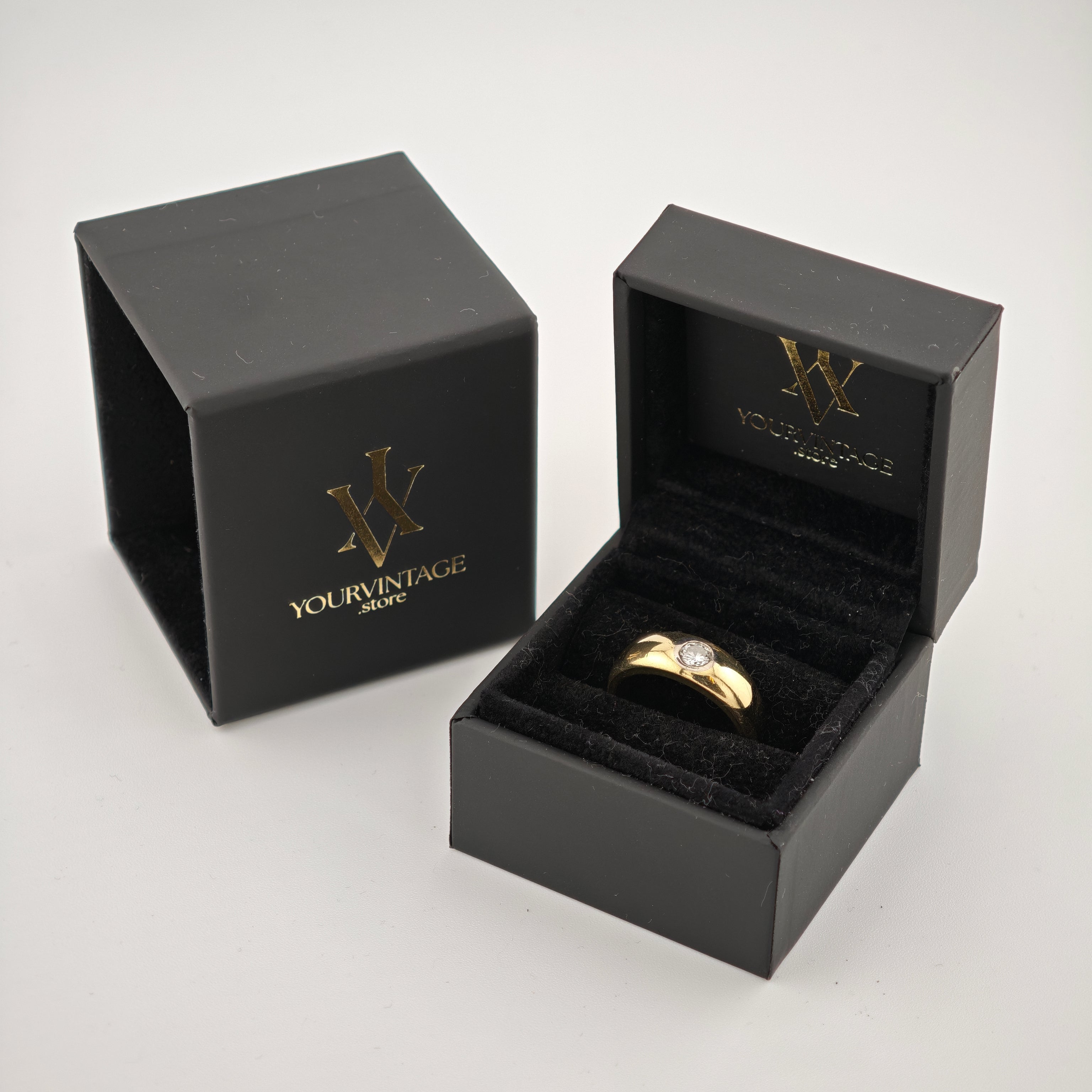 Zwei schwarze Schmuckboxen mit goldfarbenem yourvintoge.shop Logo, eine geöffnet mit goldenem Ring und klarem Edelstein.