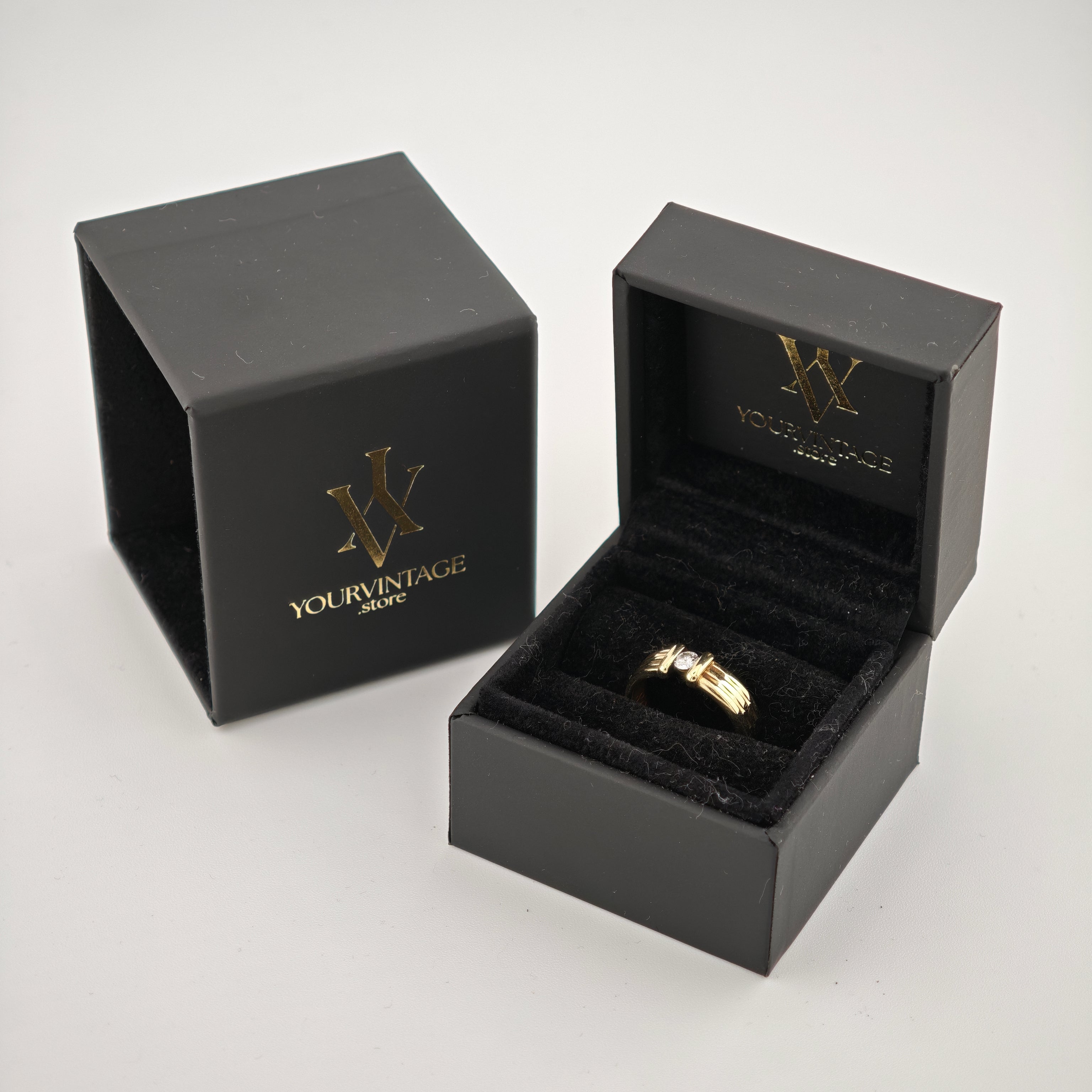 Schwarze Schmuckschachtel mit goldenem Logo und Goldring auf schwarzem Samtkissen