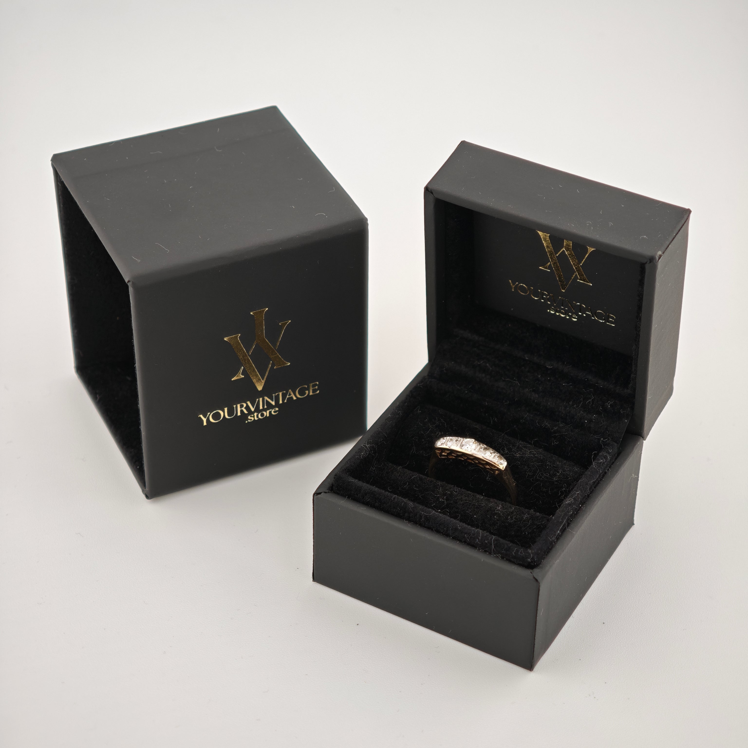 Schwarze Schmuckschachteln mit goldfarbenem WV-Logo und Diamantring auf schwarzem Samt