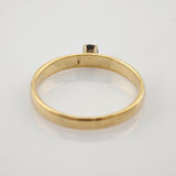 Seitliche Ansicht eines goldenen Rings mit kleinem Stein auf weißem reflektierendem Untergrund.