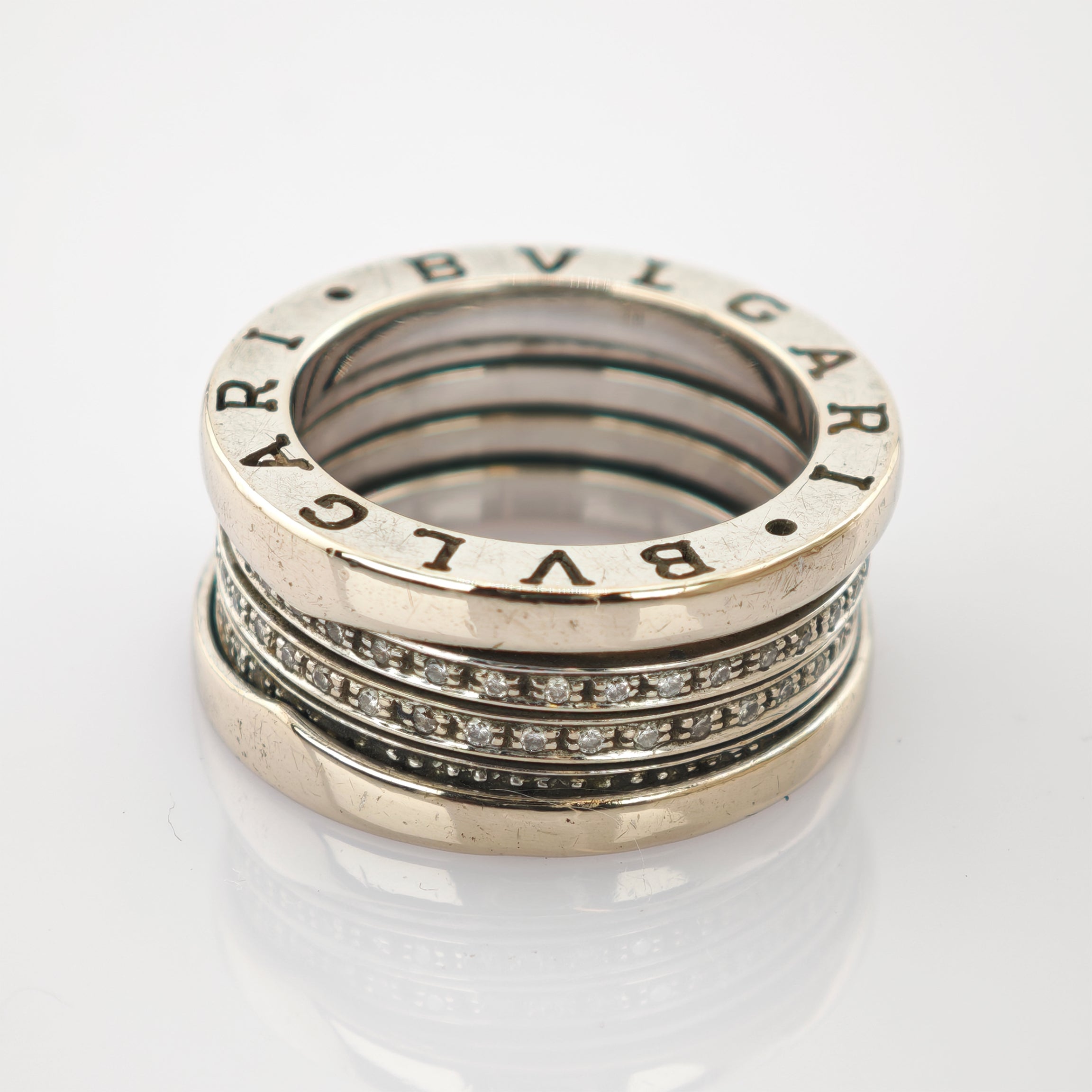 Silberner Bvlgari-Ring mit eingraviertem Markennamen und kleinen Diamanten auf reflektierender Oberfläche.