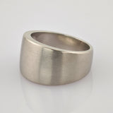 Silberner Ring mit asymmetrischem Design und matter Oberfläche auf reflektierender weißer Fläche.