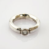 Silberner Ring mit breitem, offenem Band und einem runden Diamanten in Zargenfassung, minimalistisch und elegant.