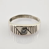 Silberner Ring mit diagonalen und vertikalen Gravuren und klarem Edelstein auf weißer Oberfläche