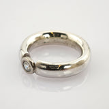 Silberner Ring mit dickem, abgerundetem Band und klarem Edelstein auf reflektierender weißer Oberfläche.