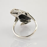 Silberner Ring in Form eines detaillierten Frosches mit realistischer Textur auf reflektierender Oberfläche.