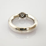 Silberner Ring mit glatter Oberfläche und schwarzem rundem Detail auf weißem reflektierendem Hintergrund.