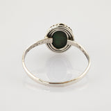 Silberner Ring mit ovalem grünen Edelstein und gerillter Fassung auf reflektierendem Untergrund