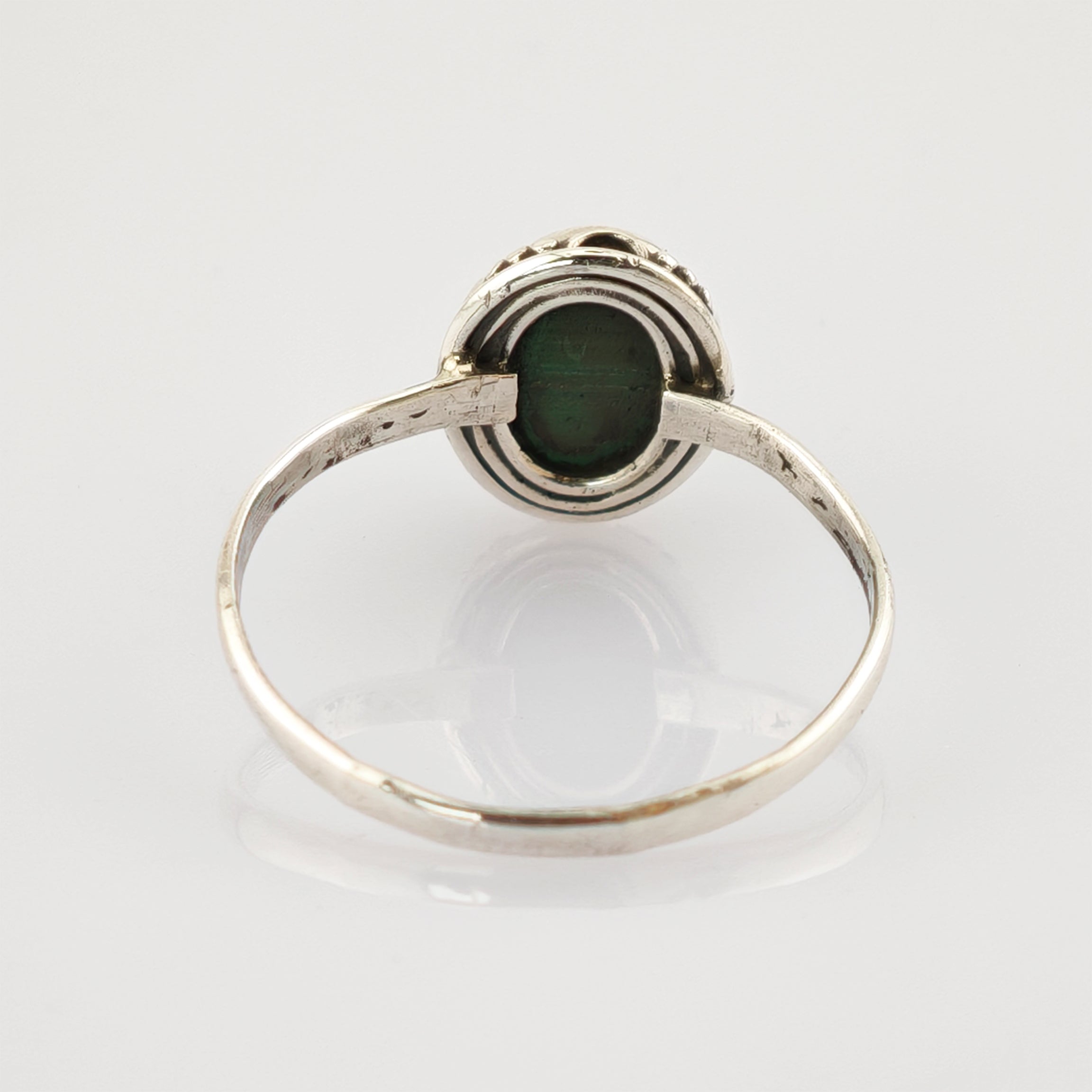Silberner Ring mit ovalem grünen Edelstein und gerillter Fassung auf reflektierendem Untergrund